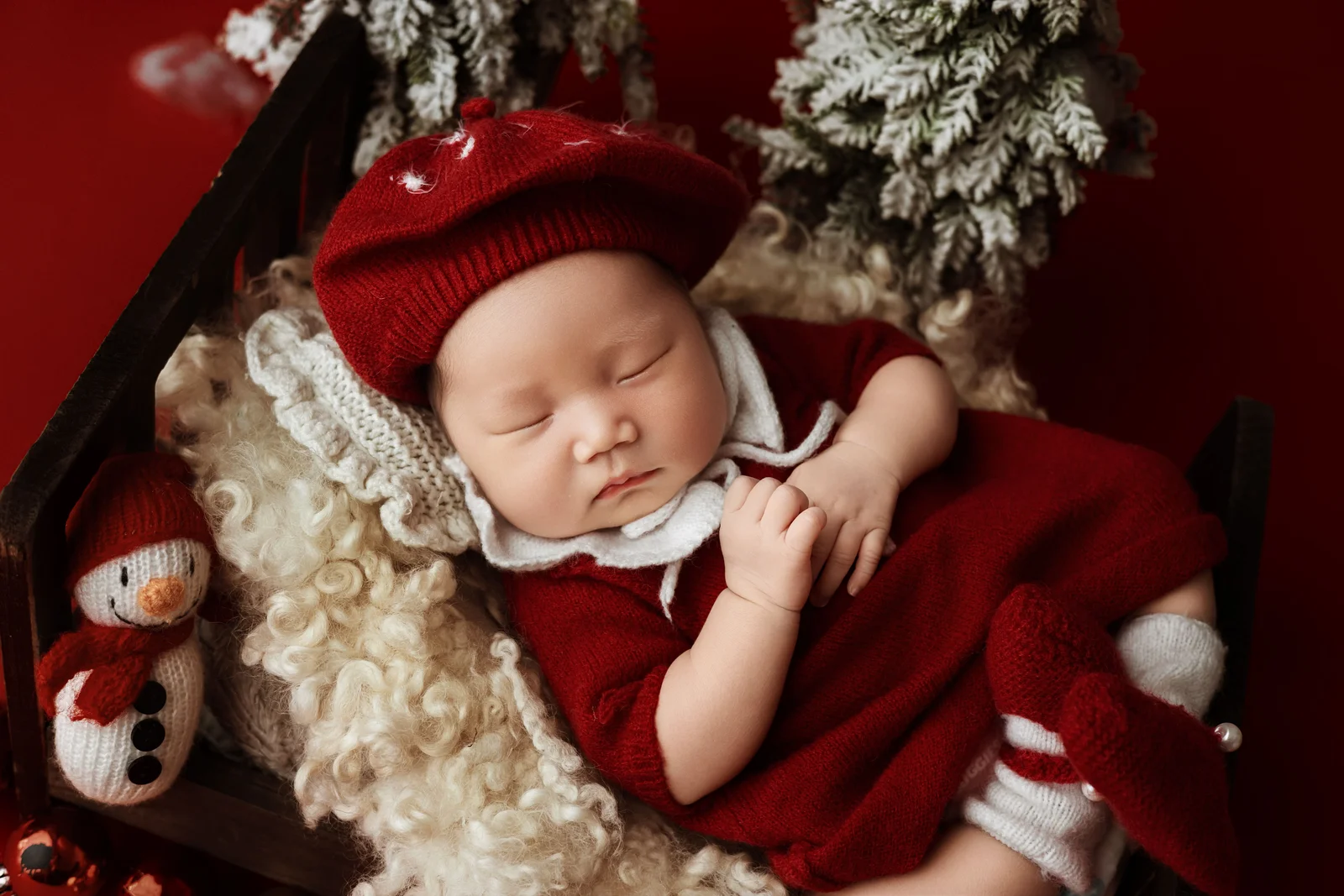 Bébé endormi en barboteuse de velours rouge et béret assorti près du sapin