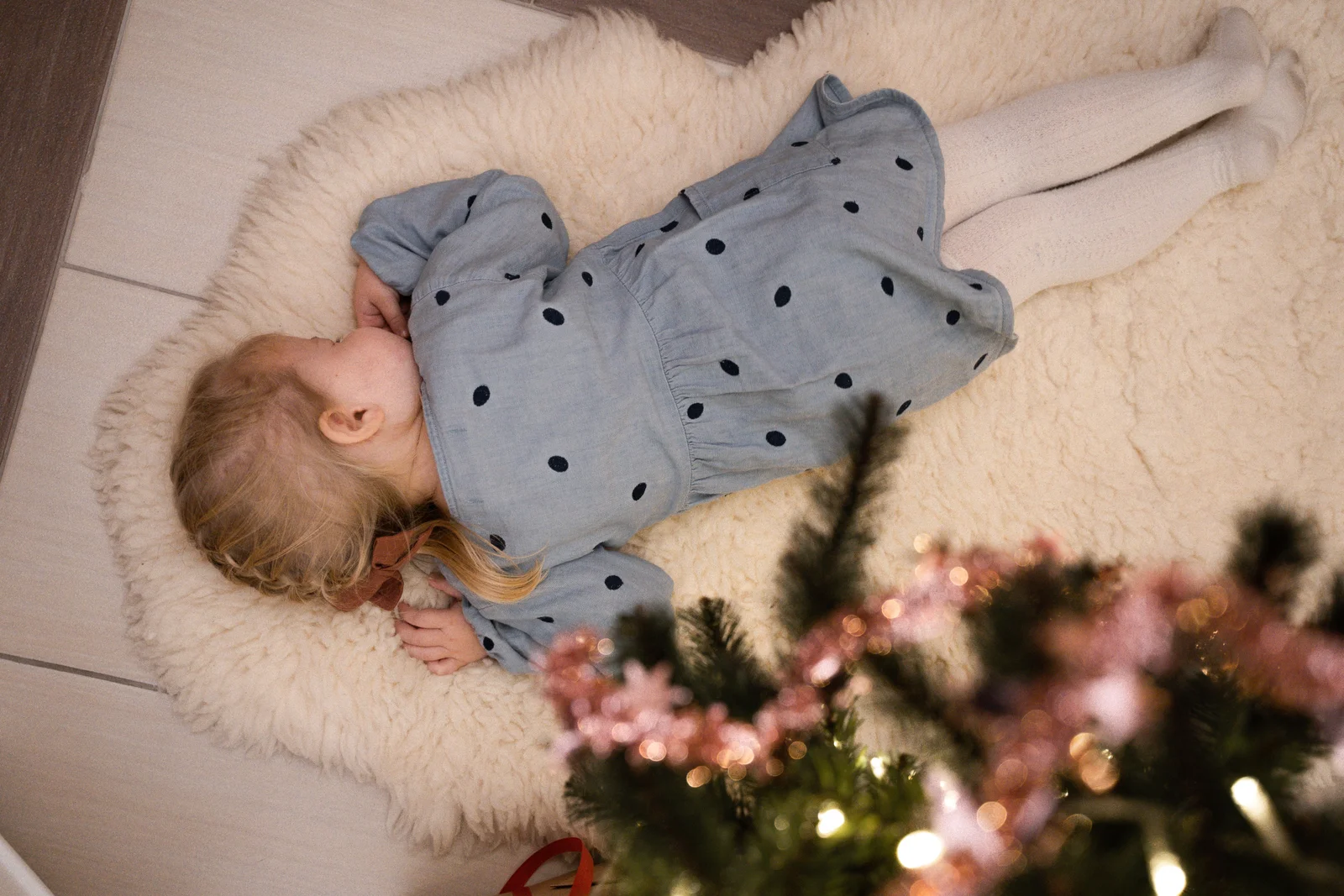 Petite fille en robe à pois et collants blancs allongée près d'une guirlande lumineuse