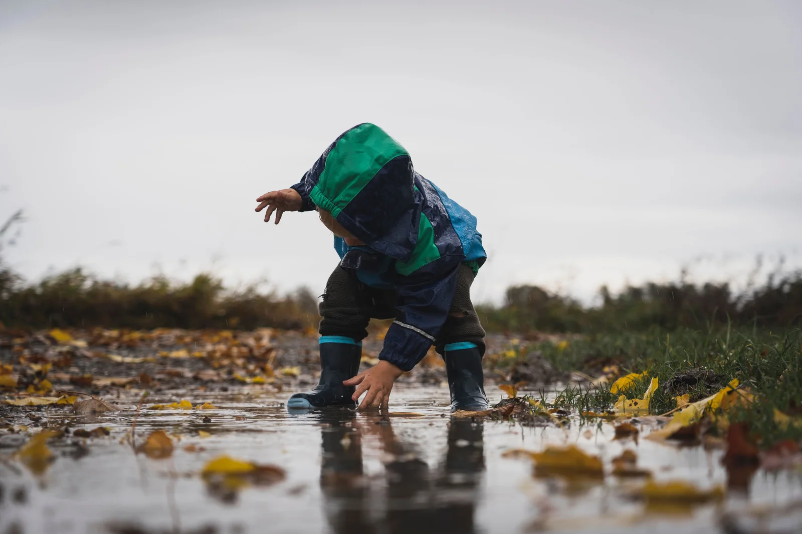 Enfant en tenue de pluie complète accroupi au bord d'une flaque en forêt