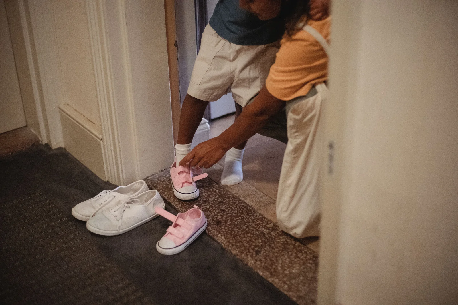 Adulte qui lace les baskets d'un enfant sur le pas de la porte