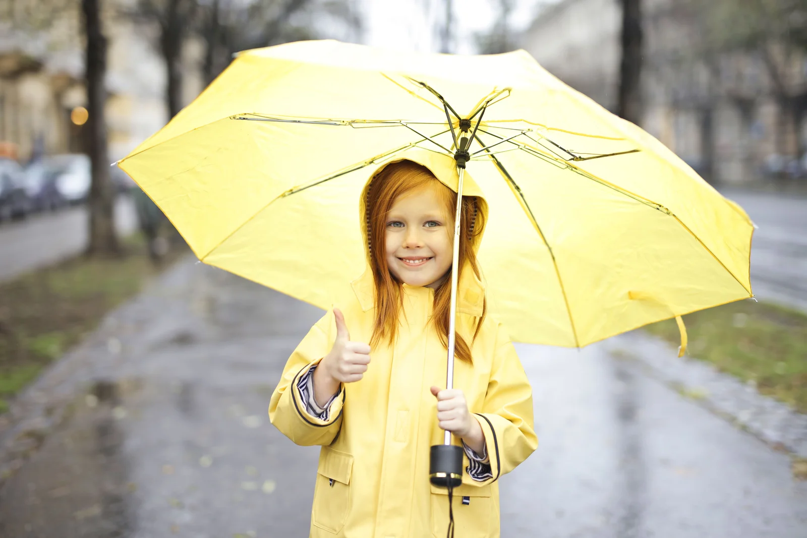 Petite fille en ciré jaune sous un parapluie jaune, sur le trajet de l'école